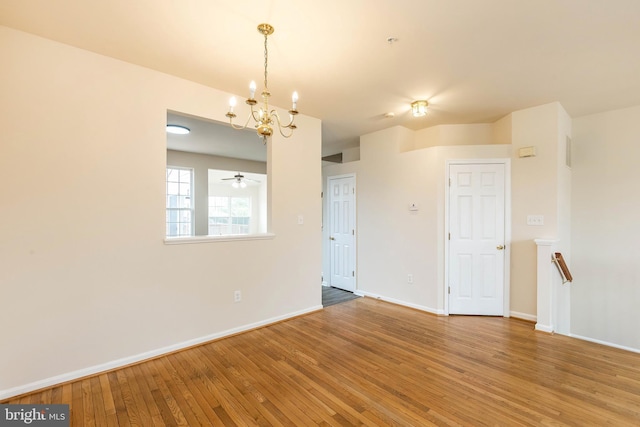 empty room featuring a notable chandelier, baseboards, and wood-type flooring