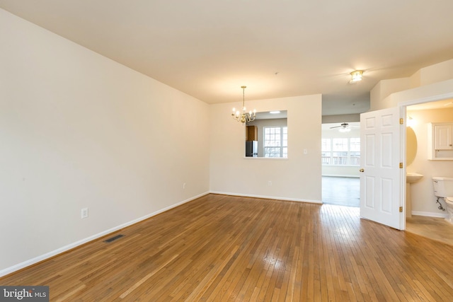 empty room with visible vents, ceiling fan with notable chandelier, baseboards, and wood-type flooring