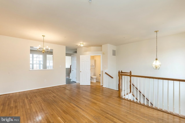 spare room with a chandelier, visible vents, baseboards, and wood-type flooring