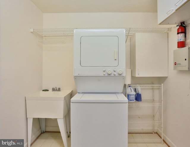 laundry area featuring stacked washer / drying machine, cabinet space, and baseboards