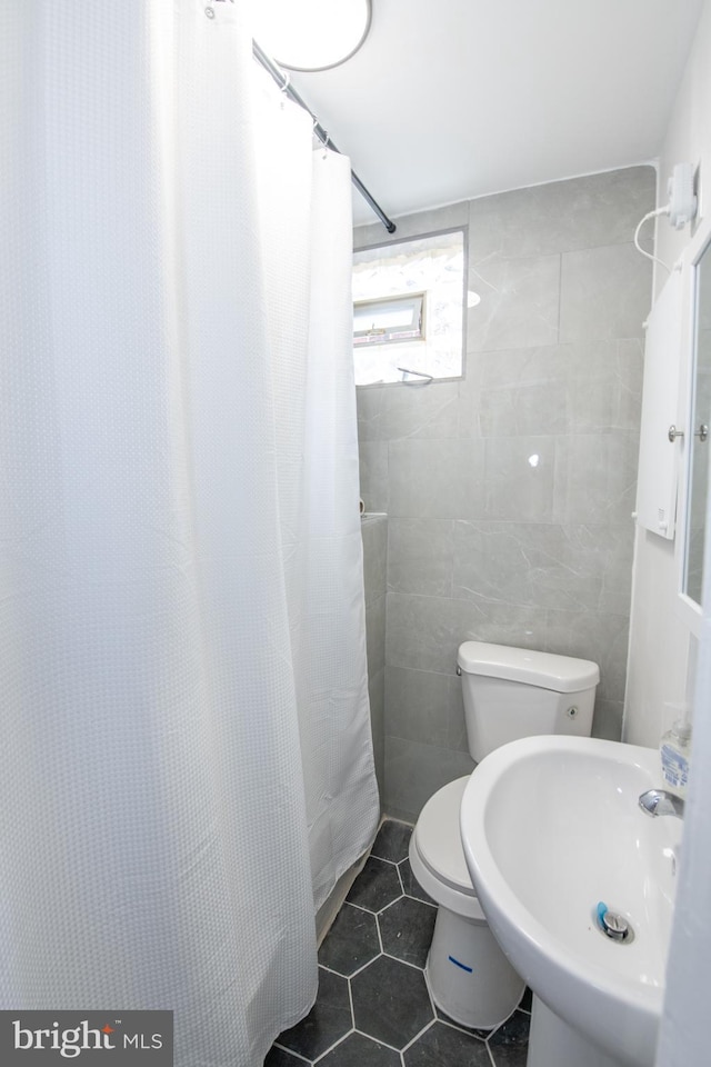 bathroom featuring toilet, a shower with shower curtain, a sink, tile walls, and tile patterned floors