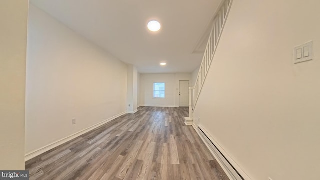 unfurnished living room with a baseboard heating unit, baseboards, and wood finished floors