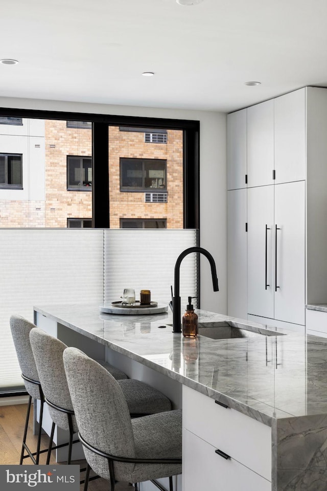 kitchen with white cabinets, a breakfast bar, wood finished floors, light stone countertops, and a sink