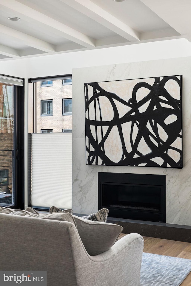 living area featuring a high end fireplace, beamed ceiling, and wood finished floors