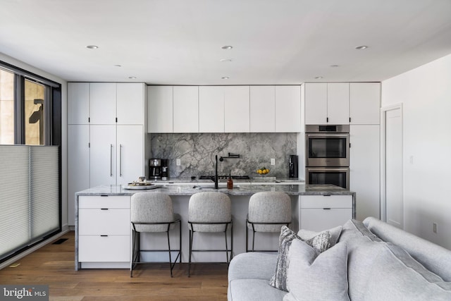 kitchen with dark stone counters, dark wood-type flooring, a kitchen island with sink, and white cabinetry