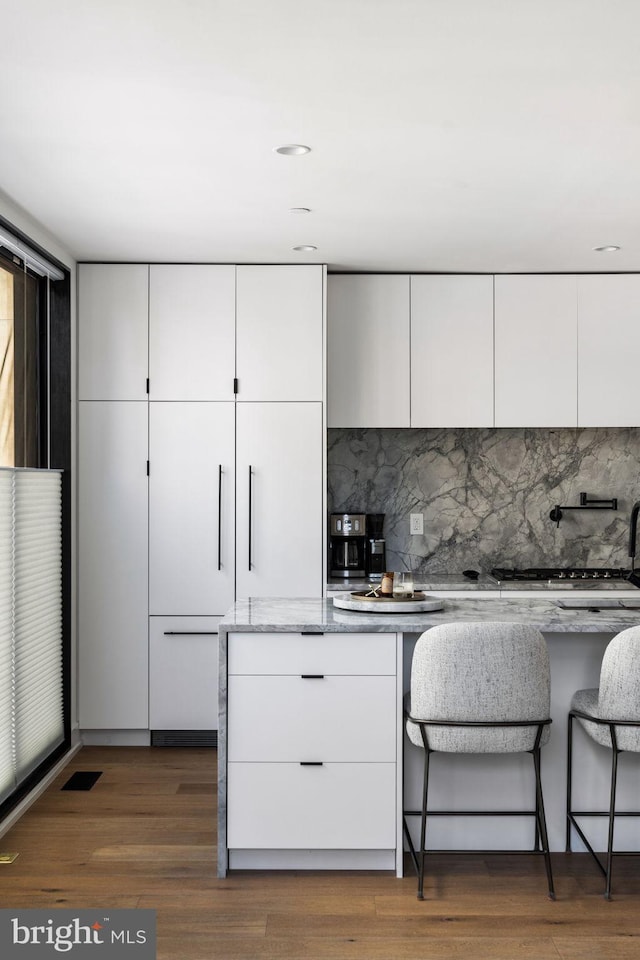 kitchen featuring dark wood-style floors, modern cabinets, decorative backsplash, white cabinetry, and light stone countertops