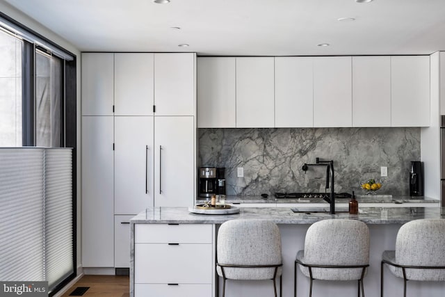 kitchen featuring light stone counters, modern cabinets, decorative backsplash, and white cabinets