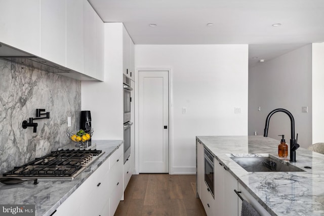 kitchen featuring light stone countertops, stainless steel appliances, white cabinets, and a sink