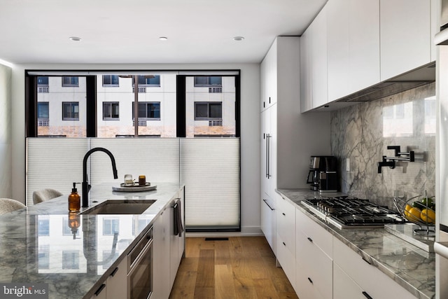 kitchen with dark stone counters, modern cabinets, stainless steel gas stovetop, white cabinetry, and a sink