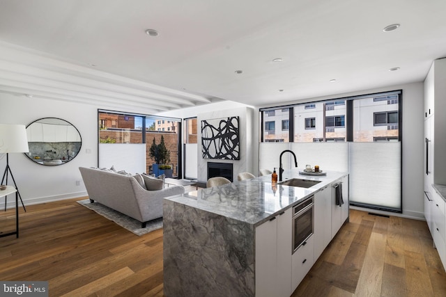 kitchen with dark wood-style flooring, wall oven, a sink, and white cabinetry