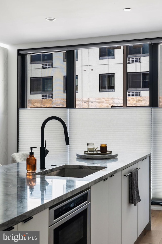 kitchen featuring oven, light stone countertops, a sink, white cabinetry, and decorative backsplash