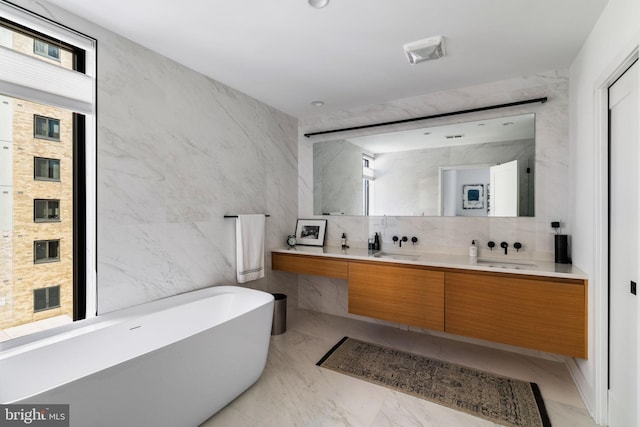 full bathroom with double vanity, tile walls, a soaking tub, marble finish floor, and a sink