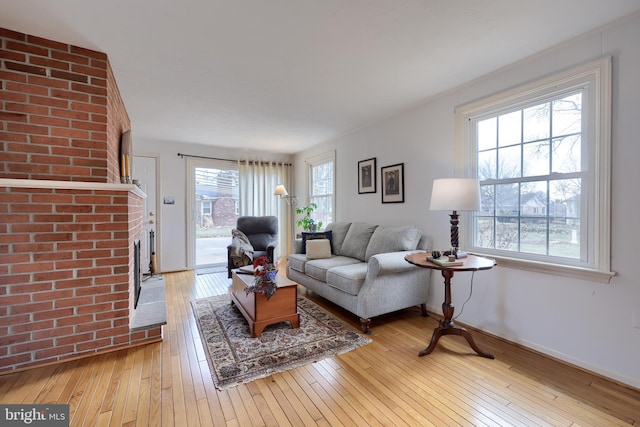 living room with light wood finished floors, a brick fireplace, and baseboards