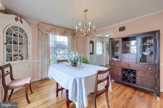 dining area with light wood-type flooring, an inviting chandelier, and crown molding