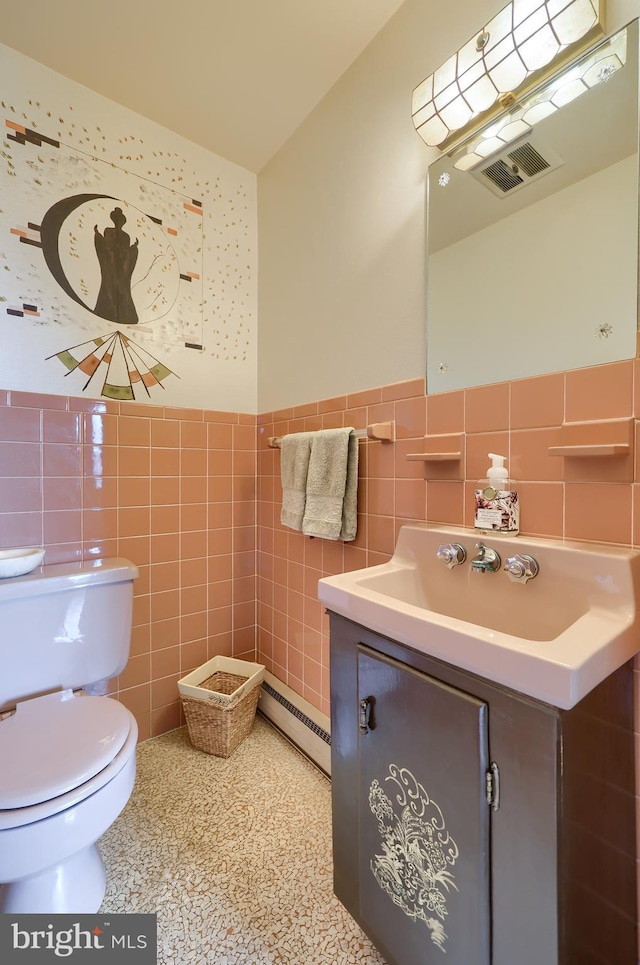 bathroom with vanity, visible vents, tile walls, baseboard heating, and wainscoting