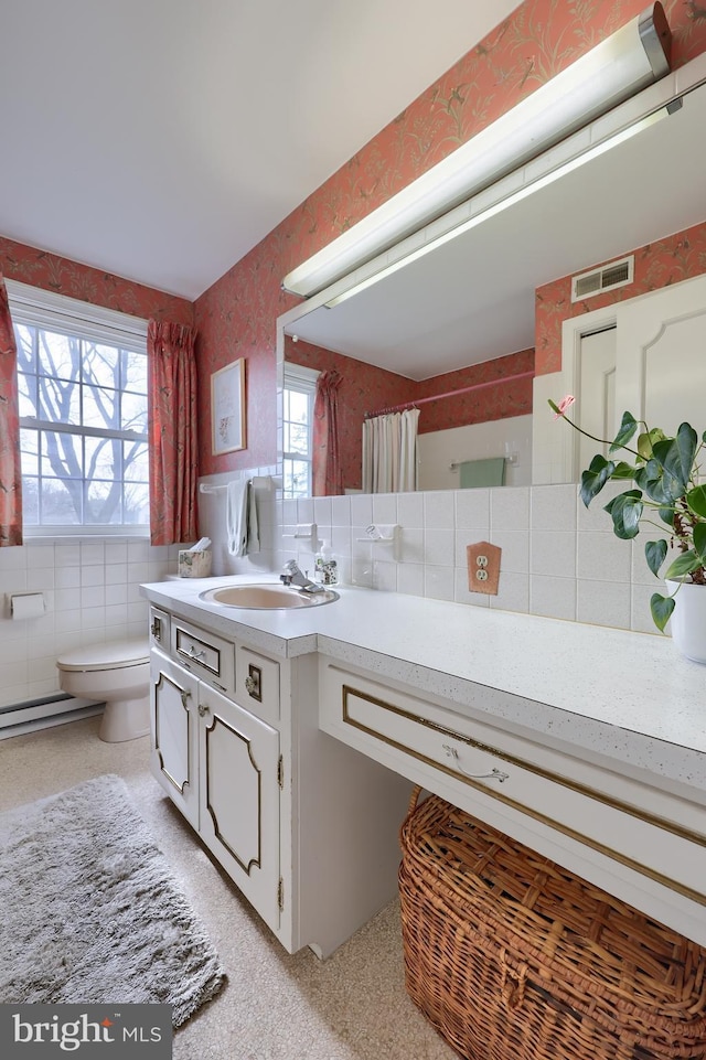 full bath with toilet, wallpapered walls, tile walls, and vanity