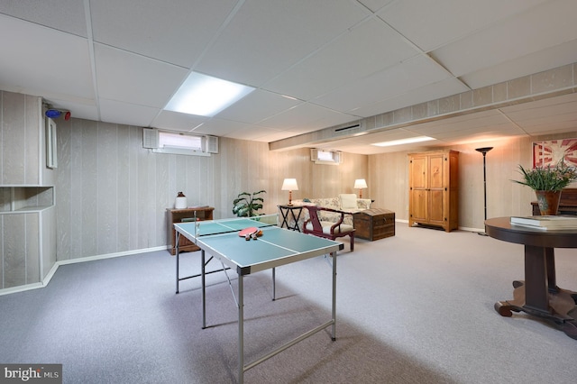 recreation room with wood walls, a drop ceiling, and baseboards