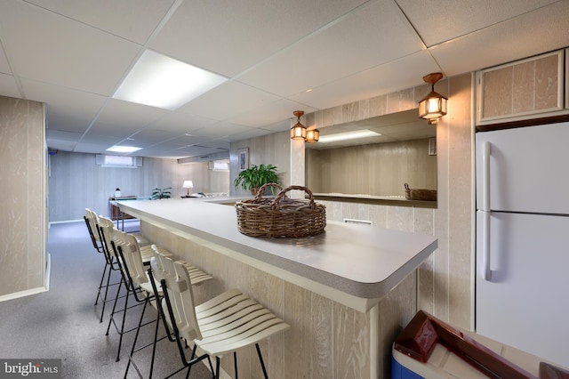 kitchen featuring freestanding refrigerator, a paneled ceiling, wood walls, and a kitchen bar