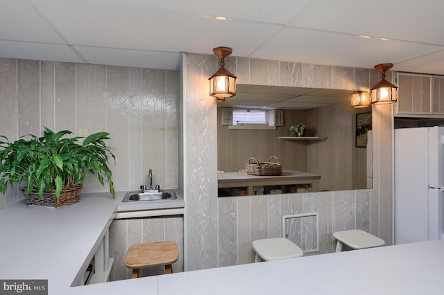 kitchen with a paneled ceiling, a sink, freestanding refrigerator, and wooden walls