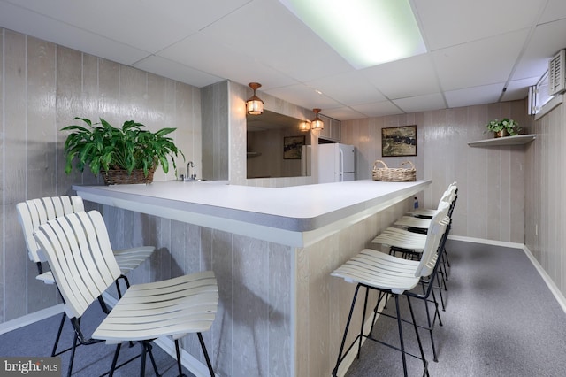 bar featuring a paneled ceiling, wooden walls, wet bar, and freestanding refrigerator