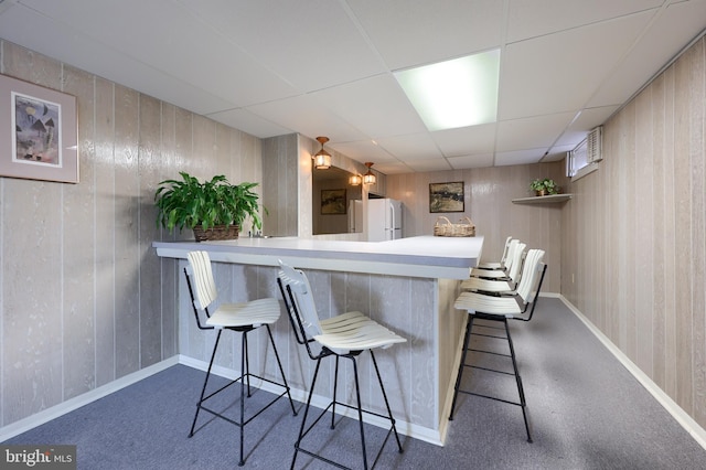 bar with wood walls, baseboards, a drop ceiling, and freestanding refrigerator