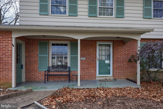 view of exterior entry with a porch and brick siding