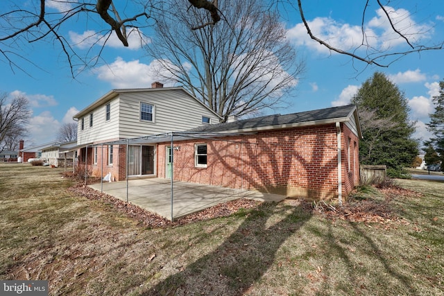 rear view of property featuring a patio area, a yard, a chimney, and brick siding