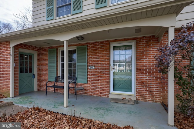 property entrance featuring covered porch and brick siding