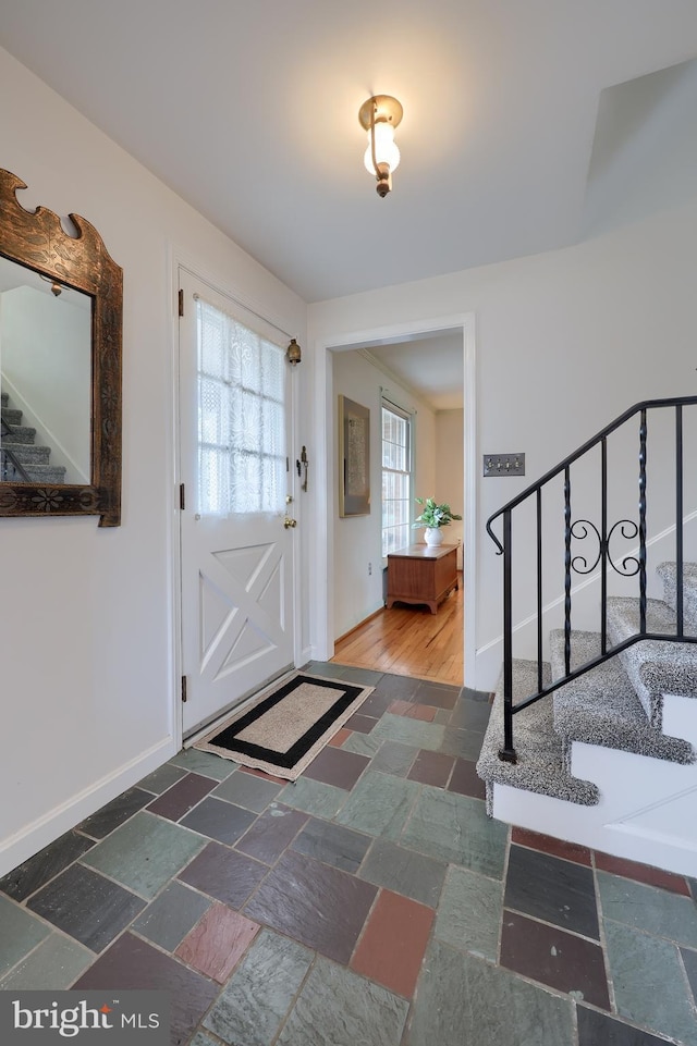 foyer entrance with baseboards, stairway, and stone tile floors