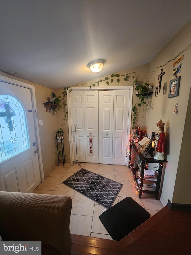 foyer entrance with light tile patterned floors, baseboards, and vaulted ceiling