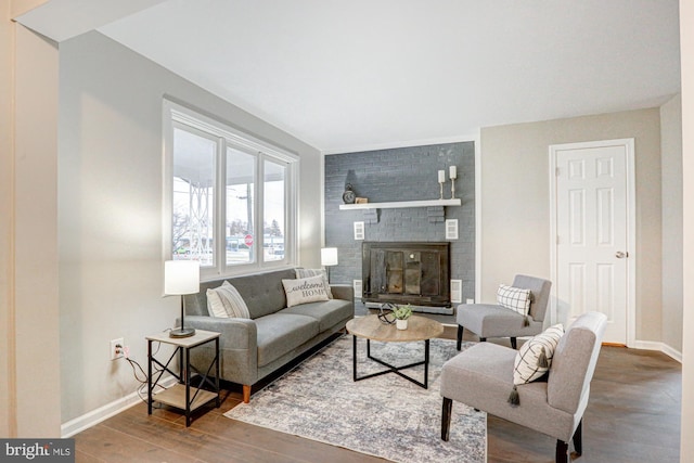 living room featuring a brick fireplace, baseboards, and wood finished floors