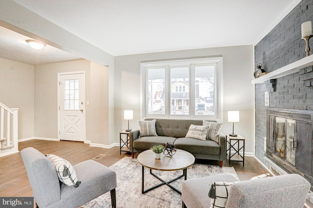 living room featuring stairway, a brick fireplace, wood finished floors, and baseboards