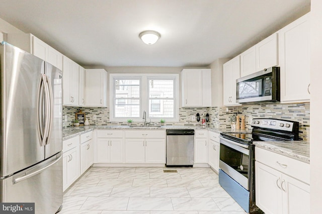 kitchen with stainless steel appliances, decorative backsplash, white cabinetry, a sink, and light stone countertops