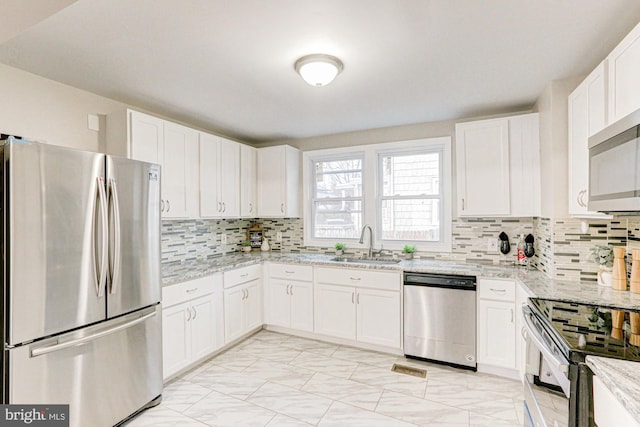 kitchen featuring stainless steel appliances, backsplash, a sink, and white cabinetry