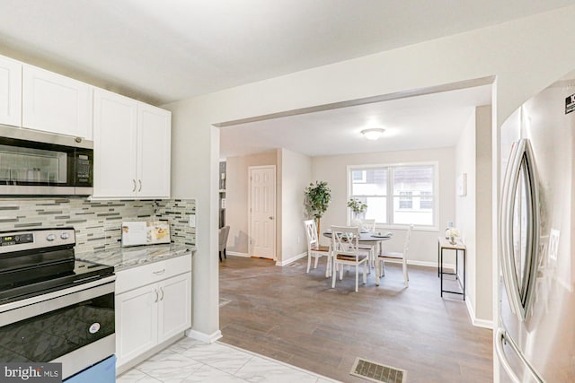 kitchen featuring visible vents, decorative backsplash, appliances with stainless steel finishes, white cabinetry, and baseboards