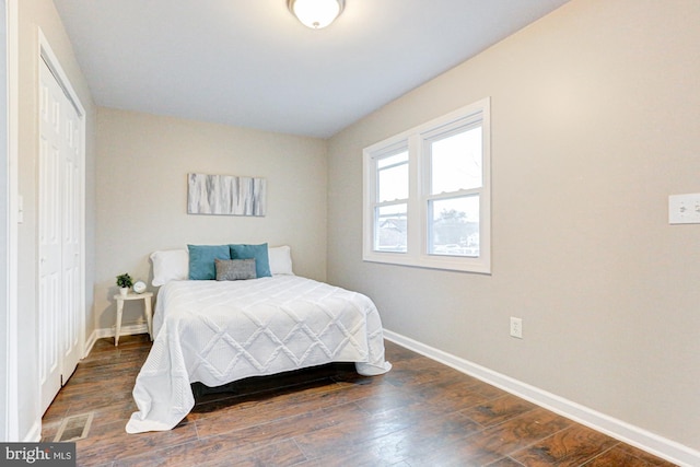 bedroom with dark wood-type flooring, a closet, and baseboards