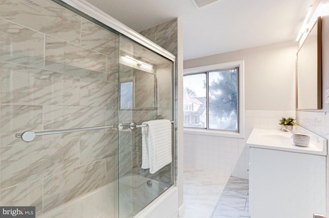 bathroom featuring shower / bath combination with glass door, a wainscoted wall, marble finish floor, vanity, and tile walls