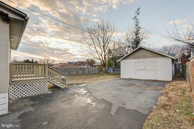 yard at dusk with a wooden deck, fence, and an outbuilding