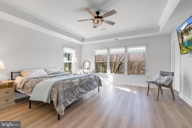 bedroom with ornamental molding, light wood-type flooring, a raised ceiling, and baseboards