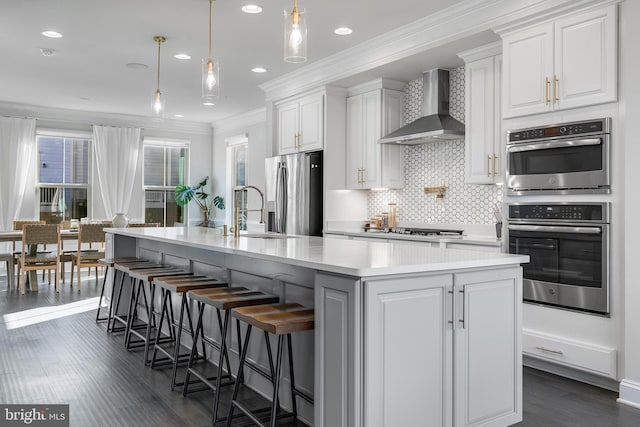 kitchen featuring stainless steel appliances, crown molding, light countertops, wall chimney range hood, and a sink