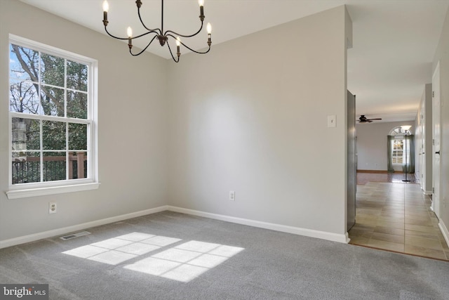 carpeted spare room featuring ceiling fan with notable chandelier, visible vents, and baseboards