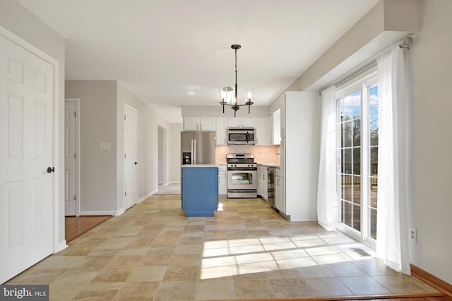 kitchen featuring stainless steel appliances, white cabinetry, light countertops, a center island, and decorative light fixtures