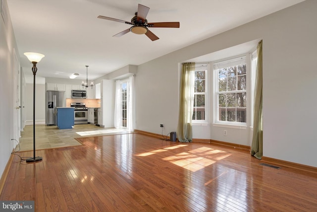 unfurnished living room featuring light wood-type flooring, baseboards, visible vents, and ceiling fan with notable chandelier