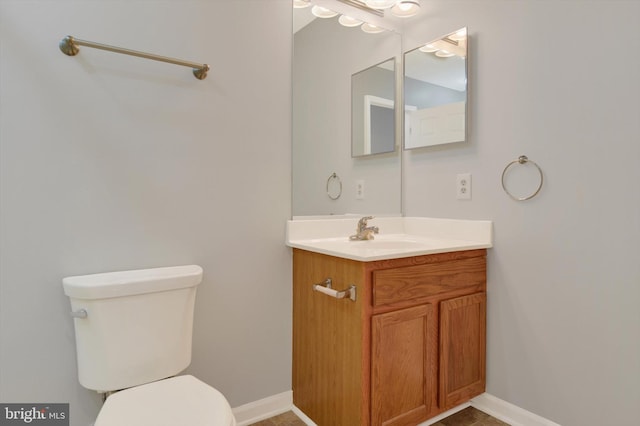 half bathroom with vanity, toilet, and baseboards