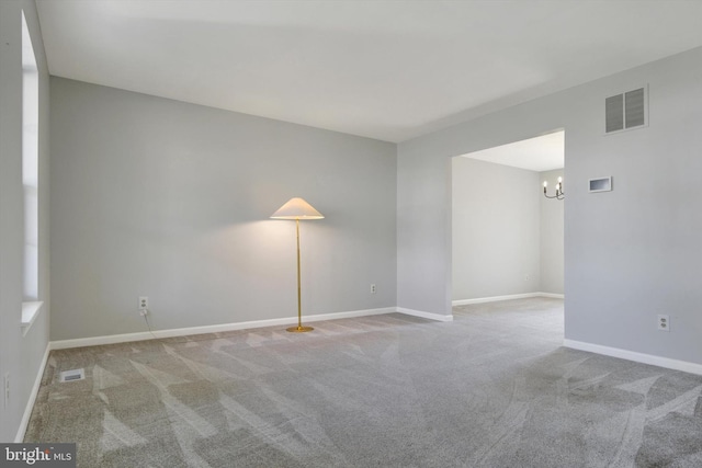 carpeted empty room with a chandelier, visible vents, and baseboards