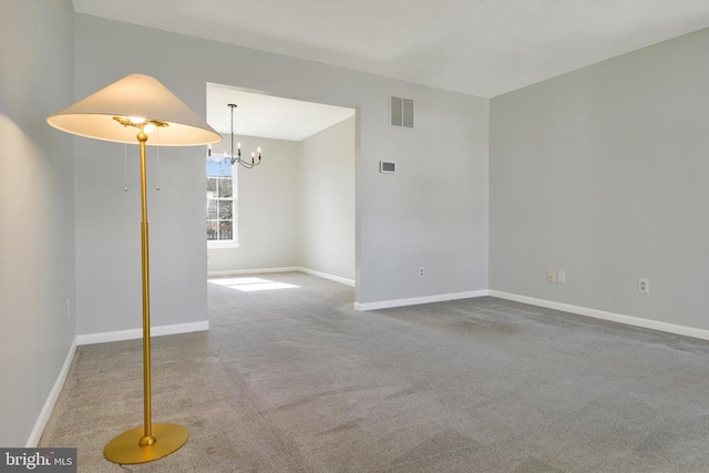 carpeted spare room with visible vents, a notable chandelier, and baseboards