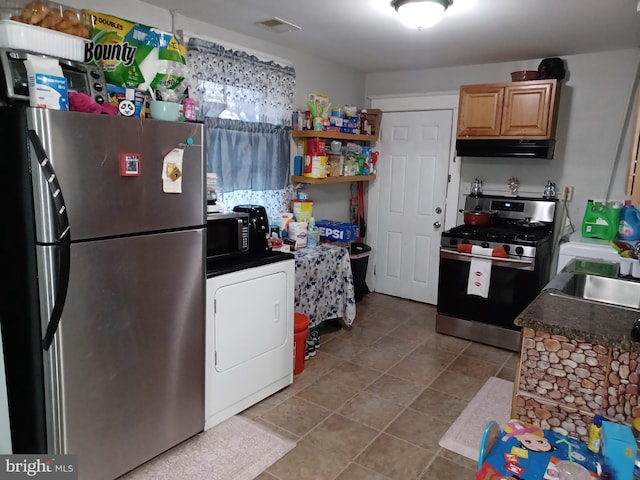 kitchen with dark countertops, appliances with stainless steel finishes, a sink, washer / dryer, and under cabinet range hood