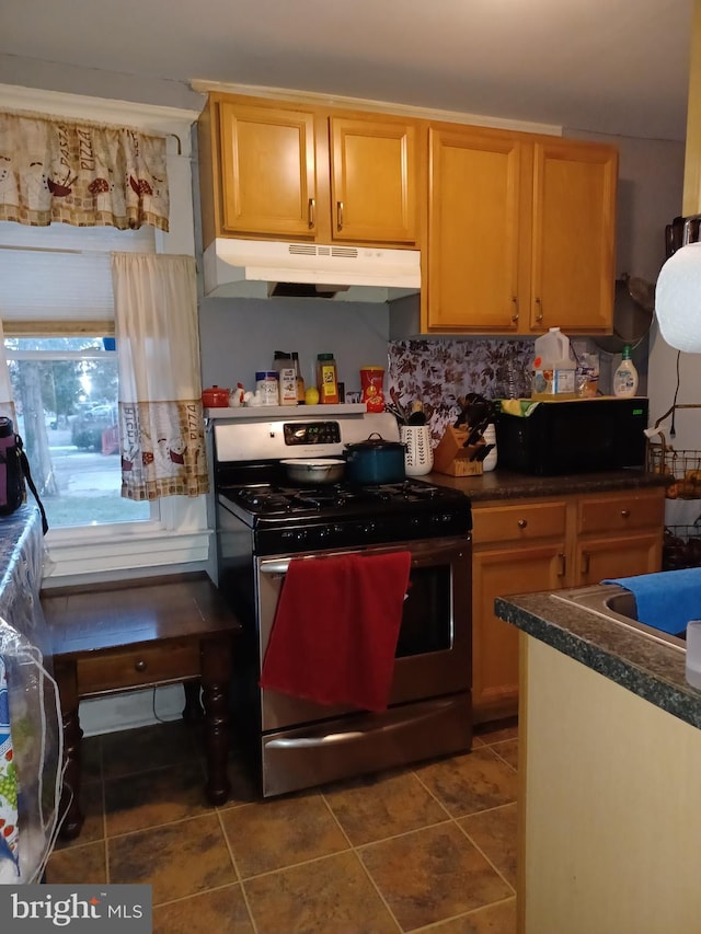 kitchen featuring stainless steel gas stove, dark tile patterned flooring, dark countertops, and under cabinet range hood