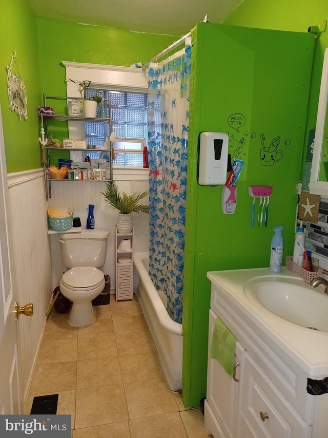 bathroom with toilet, a wainscoted wall, a sink, tile patterned floors, and shower / bathtub combination with curtain