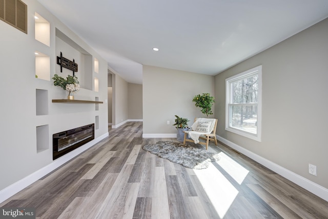 unfurnished room featuring a glass covered fireplace, wood finished floors, visible vents, and baseboards